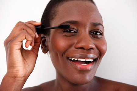 Close up portrait of smiling beautiful african woman putting on make up on her eyeの写真素材