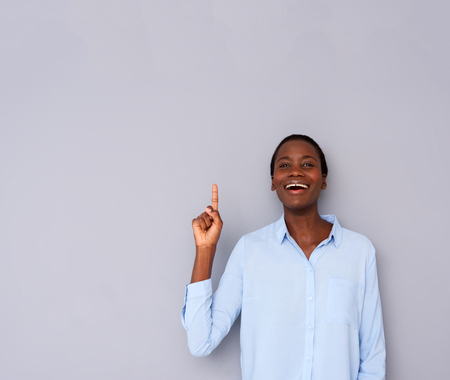 Portrait of smiling black woman in shirt pointing up on gray backgroundの写真素材