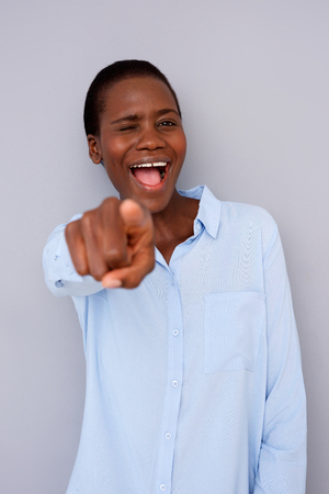 Portrait of excited black woman pointing finger in front laughing and winking on gray backgroundの写真素材