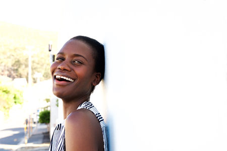 Horizontal portrait of laughing young african american lady leaning to a wall outdoorsの写真素材