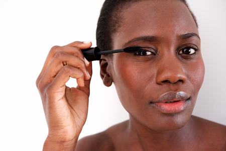 Close up portrait of young black woman putting make up on eye against white backgroundの写真素材