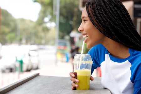 Side portrait of young african woman with braided hair sipping juice at cafeの写真素材
