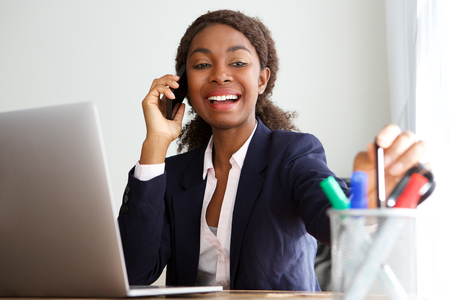 Portrait of happy african businesswoman talking on mobile phone in officeの写真素材