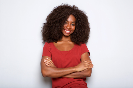 Close up portrait of smiling young african woman standing with arms crossed against white backgroundの写真素材