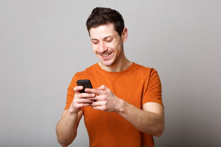 Portrait of smiling young man looking at text message on mobile phoneの写真素材