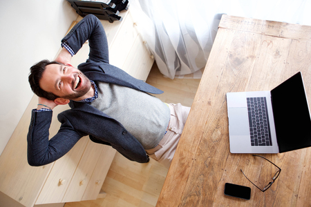 Portrait of happy businessman relaxing in office with laptopの写真素材