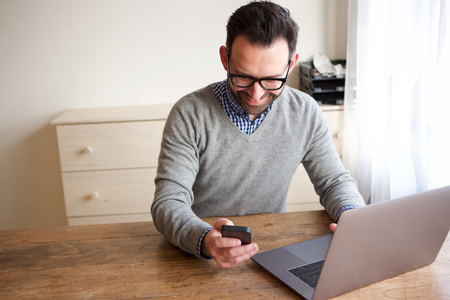 Portrait of happy businessman working with laptop computer and looking at mobile phoneの写真素材