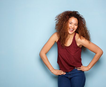 Portrait of young woman with curly hair laughing by blue background