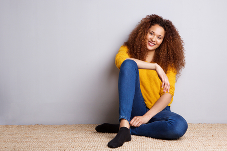 Portrait of african american girl sitting on floor and smiling by gray wallの写真素材