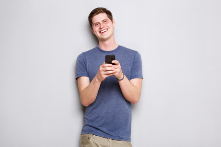 Portrait of happy young man standing by wall with mobile phone