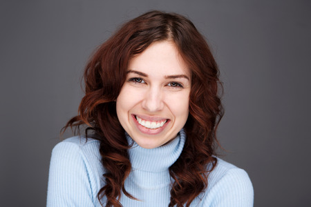 Close up front portrait of happy young woman smiling against gray background