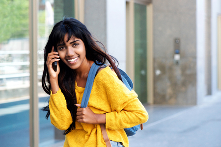 Portrait of smiling young Indian woman walking and talking with mobile phoneの写真素材
