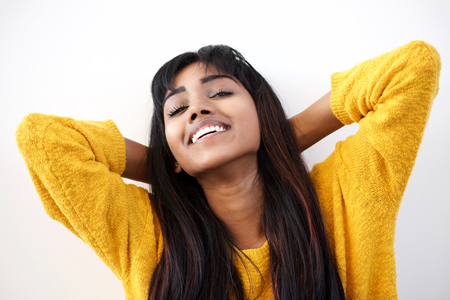 Close up portrait of smiling young Indian woman with hands behind head against white backgroundの写真素材