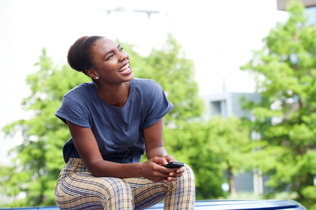 Portrait of beautiful young african american woman laughing with mobile phone outdoorsの写真素材