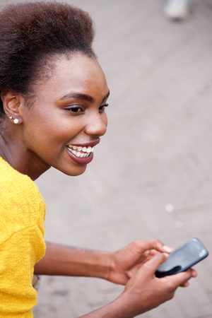 Close up portrait of smiling young black woman with cellphone outsideの写真素材