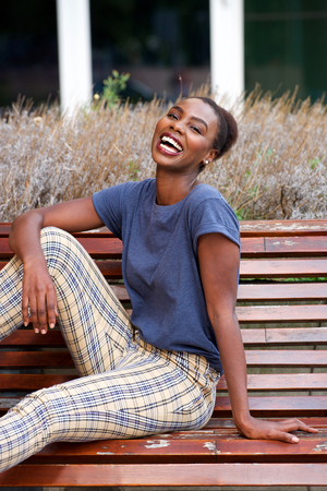 Portrait of young woman sitting on bench outside and laughingの写真素材