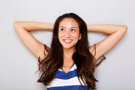 Close up portrait of smiling young asian woman with hands behind head against gray backgroundの写真素材