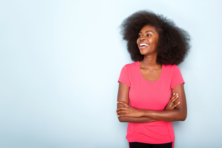 Portrait of smiling young black woman with arms crossed against blue backgroundの写真素材