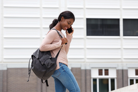 Side portrait of smiling young black woman with bag and mobile phoneの写真素材