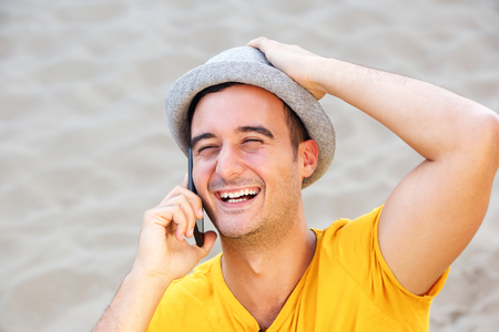 Close up portrait of happy man with hat talking on mobile phone at the beachの写真素材