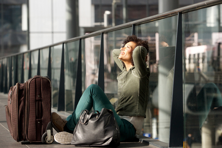 Portrait of african american travel woman sitting on station floor with suitcase bagsの写真素材