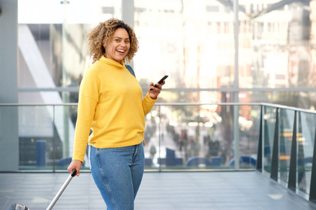 Portrait of happy travel woman with cellphone at stationの写真素材