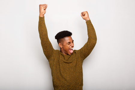 Portrait of happy young black man with arms raised in joy against gray backgroundの写真素材