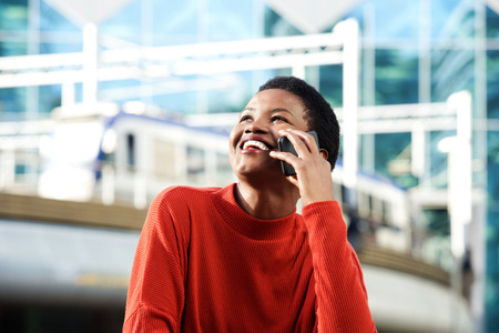 Portrait of smiling young african woman talking on cellphone in city