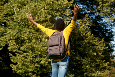 Portrait from behind of young black woman with arms outstretched in parkの写真素材