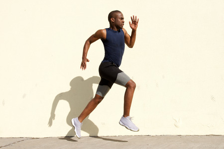 Full body side portrait of healthy young black man running by wall
