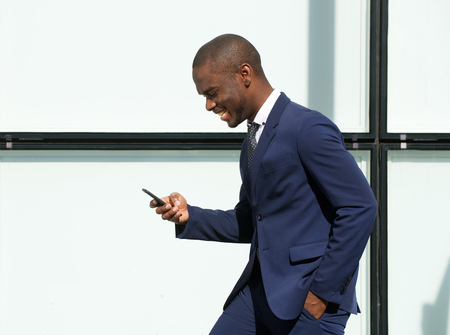 Side portrait of happy african american corporate businessman walking with cellphone in cityの写真素材