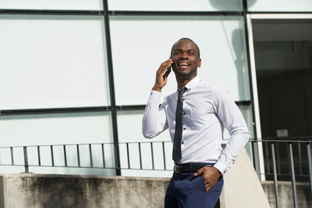 Portrait of african american businessman walking and talking with mobile phone in the cityの写真素材