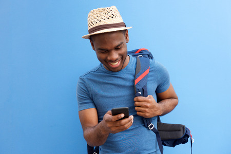 Portrait of cool young african american guy with bag and cellphone against blue backgroundの写真素材