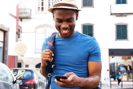 Portrait of happy young male tourist walking with mobile phone and bag in the cityの写真素材