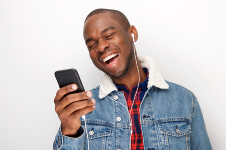 Close up portrait of happy young african american guy listening to music with smart phone and earphonesの写真素材