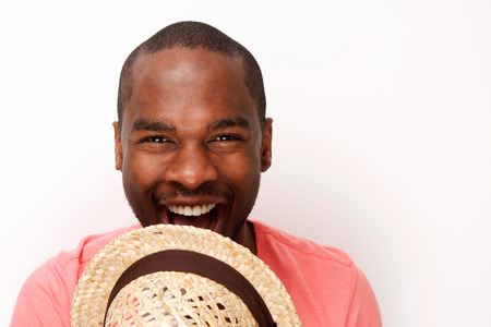 Close up portrait of cheerful young black man laughing with hat bye white wallの写真素材