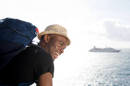 Side portrait of handsome young african american travel man smiling by the sea with cruise ship in backgroundの写真素材