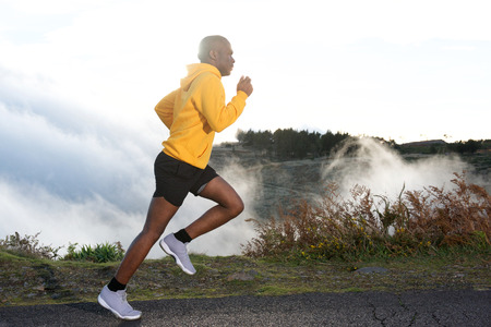 Full body side portrait of young black man road running in nature