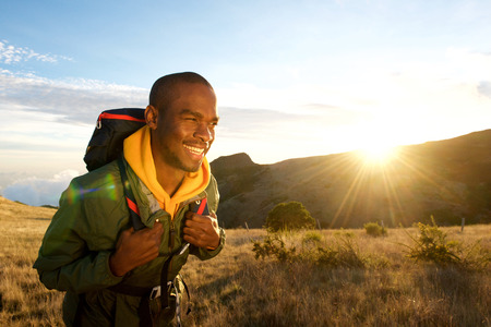 Portrait of young black man walking with backpack in mountains with sunrise in backgroundの写真素材