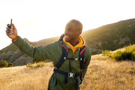 Portrait of handsome young african american male hiker taking selfie with cellphone in natureの写真素材