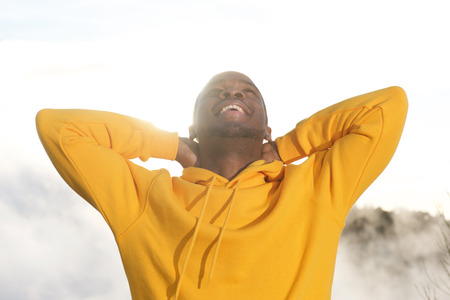 Close up portrait of handsome young african american man smiling with hands behind head and sun in...