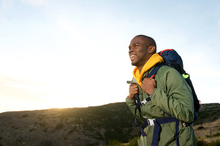 Side portrait of happy african american man hiking in nature with backpackの写真素材