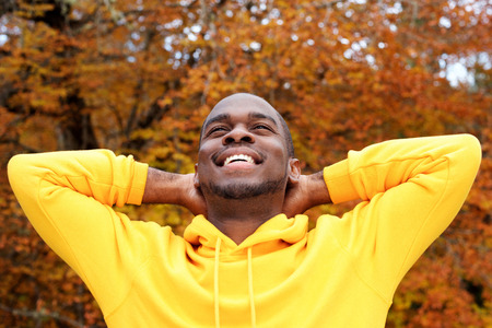 Close up portrait of handsome young african american man against autumn leaves in background smiling...