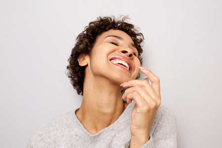 Close up portrait of happy young woman laughing with hand by head against white wallの写真素材