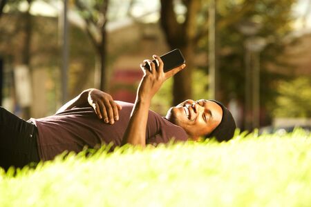 Portrait of happy african american man relaxing in park and looking at mobile phoneの写真素材