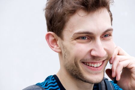 Close up portrait of young man smiling and talking with mobile phone by white background