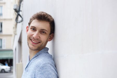 Side portrait of young man leaning against wall and smiling