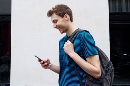 Side portrait of young man walking with mobile phone and bag