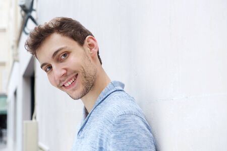 Close up side portrait of young man leaning against wall and smiling