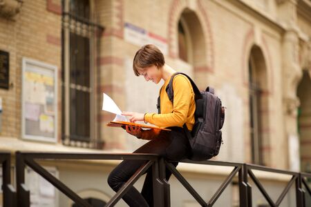 Side portrait of female student sitting on campus reading book